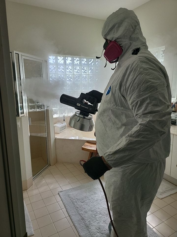 Technician in full PPE using thermal fogger in bathroom for smoke odor elimination